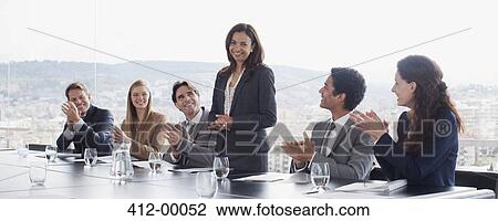 Stock Image - Co-workers clapping for businesswoman in conference room. Fotosearch