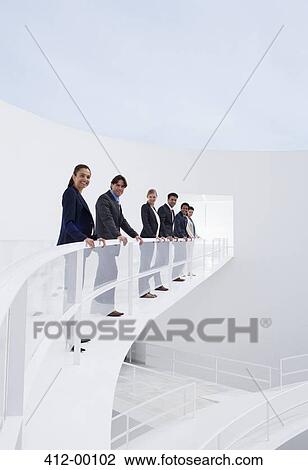 Portrait of smiling business people leaning on railing of elevated walkway View Large Photo Image Stock Image - Portrait of smiling business people leaning on railing of elevated walkway. Fotosearch