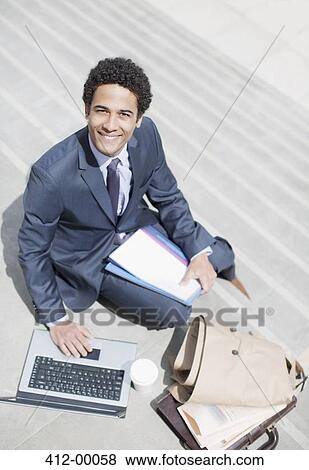 Portrait of smiling businessman with paperwork using laptop on sunny stairs View Large Photo Image Stock Photo - Portrait of smiling businessman with paperwork using laptop on sunny stairs. Fotosearch