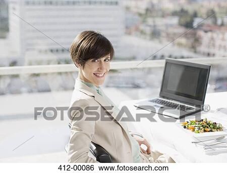 Stock Photograph - Portrait of smiling businesswoman with lunch at desk. Fotosearch