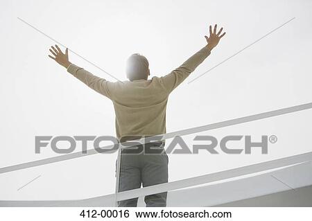 Stock Photograph - Sun shining behind businessman with arms raised. Fotosearch