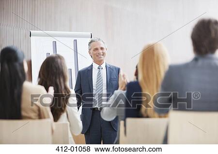 Stock Photo - Business people applauding businessman standing at flipchart. Fotosearch