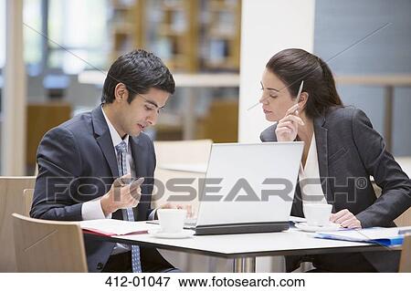 Stock Photo - Businessman and businesswoman reviewing paperwork at cafe. Fotosearch