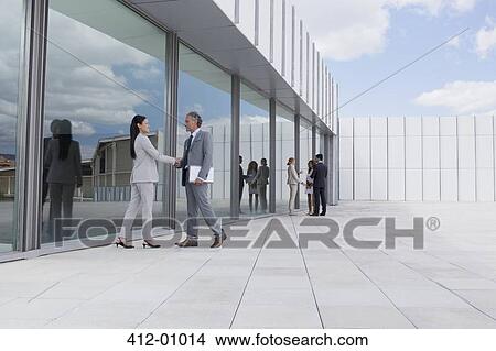 Picture - Businessman and businesswoman shaking hands outside building. Fotosearch