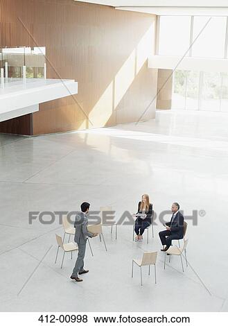 Stock Photo - Businessman approaching co-workers at circle of chairs. Fotosearch