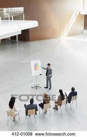 Businessman at flipchart leading meeting in modern lobby View Large Photo Image Stock Photo - Businessman at flipchart leading meeting in modern lobby. Fotosearch