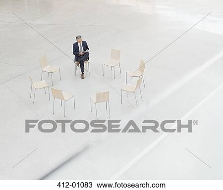 Businessman reviewing paperwork at circle of chairs in lobby View Large Photo Image Stock Image - Businessman reviewing paperwork at circle of chairs in lobby. Fotosearch