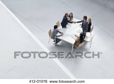 Stock Photograph - Businessmen in meeting shaking hands across table. Fotosearch