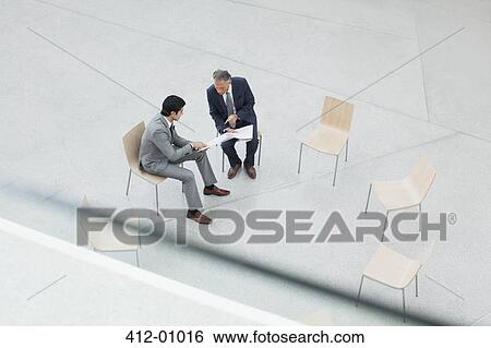 Stock Photograph - Businessmen reviewing paperwork in circle of chairs. Fotosearch