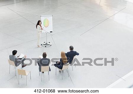 Stock Photo - Businesswoman at flipchart leading meeting in lobby. Fotosearch