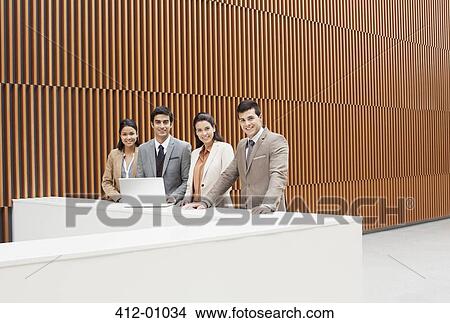 Picture - Portrait of confident business people with laptop at ledge in office. Fotosearch
