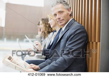Portrait of confident businessman reading newspaper with co-workers in background View Large Photo Image Stock Photo - Portrait of confident businessman reading newspaper with co-workers in background. Fotosearch