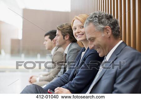 Stock Image - Portrait of smiling businesswoman sitting with businessmen. Fotosearch
