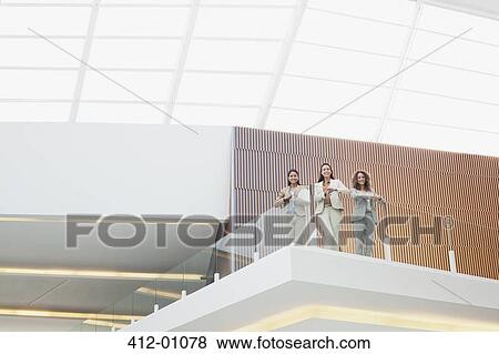 Portrait of smiling businesswomen standing on balcony in modern office View Large Photo Image Stock Photo - Portrait of smiling businesswomen standing on balcony in modern office. Fotosearch