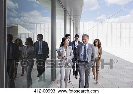 Stock Image - Smiling business people walking along building. Fotosearch