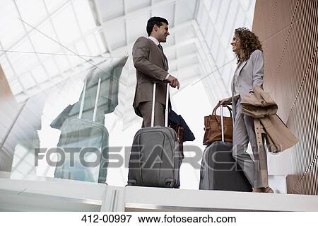 Stock Photo - Smiling businessman and businesswoman with suitcases talking in airport. Fotosearch