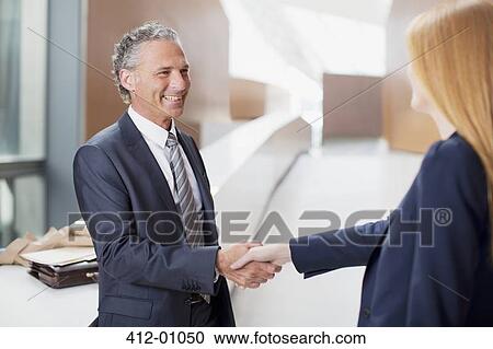 Stock Image - Smiling businessman shaking hands with businesswoman. Fotosearch