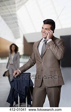 Stock Image - Smiling businessman talking on cell phone at airport. Fotosearch