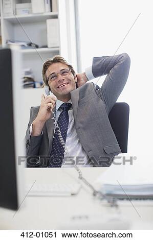 Smiling businessman talking on telephone at desk in office View Large Photo Image Stock Image - Smiling businessman talking on telephone at desk in office. Fotosearch