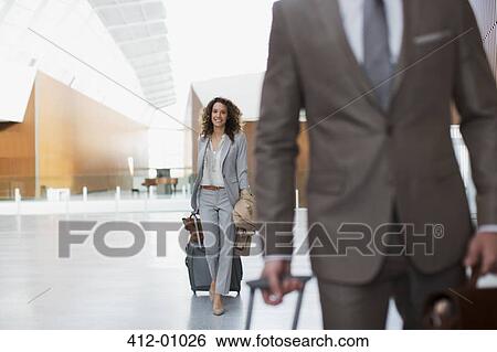 Stock Photograph - Smiling businesswoman pulling suitcase in airport. Fotosearch
