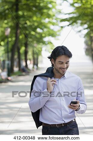 Stock Photo - Businessman checking cell phone in park. Fotosearch