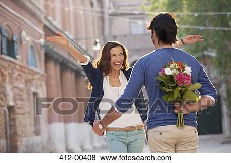Enthusiastic woman approaching man with flowers behind back View Large Photo Image Stock Photo - Enthusiastic woman approaching man with flowers behind back. Fotosearch