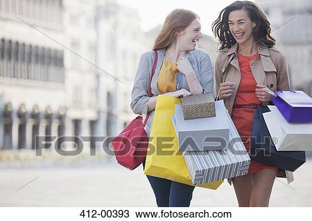Stock Image - Happy women with shopping bags walking through town square. Fotosearch