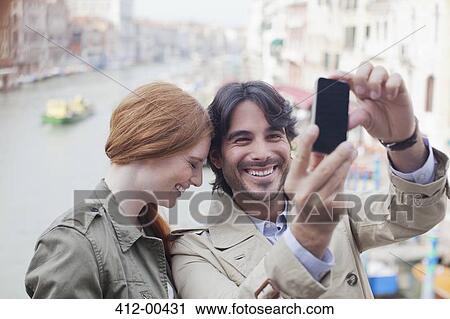 Stock Image - Laughing couple taking self-portrait with camera phone on canal in Venice. Fotosearch