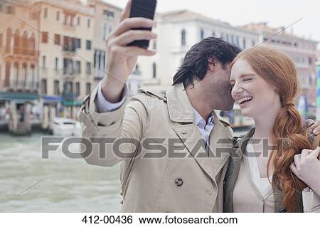 Stock Photograph - Laughing couple taking self-portrait with camera phone at waterfront in Venice. Fotosearch