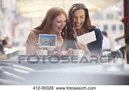 Laughing friends looking at postcards at sidewalk cafe View Large Photo Image Stock Photo - Laughing friends looking at postcards at sidewalk cafe. Fotosearch
