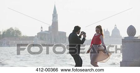 Stock Photograph - Man filming woman at waterfront in Venice. Fotosearch
