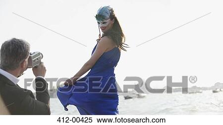 Stock Photography - Man filming woman in mask at waterfront in Venice. Fotosearch