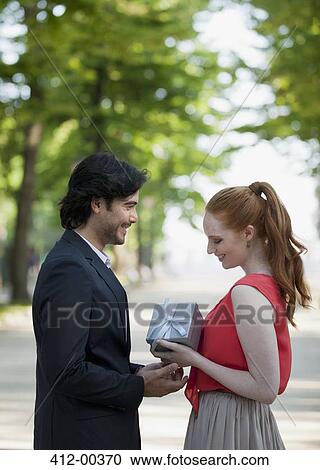Stock Image - Man giving woman gift in park. Fotosearch