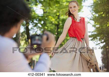 Stock Image - Man photographing woman in park. Fotosearch