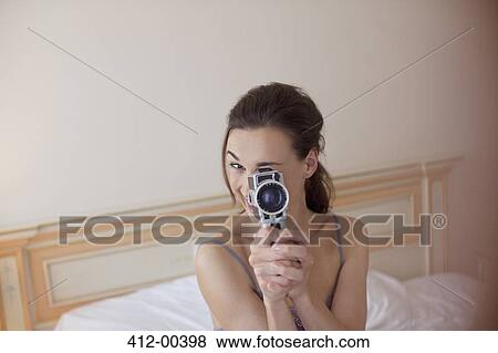 Stock Photo - Portrait of woman holding old-fashioned video camera in bed. Fotosearch