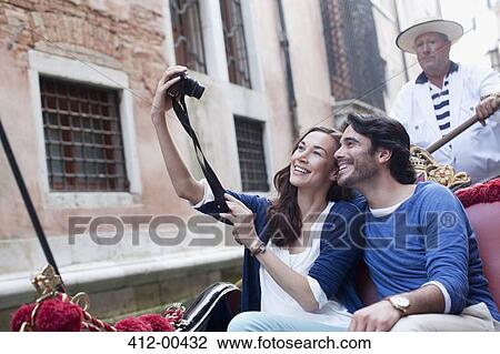 Stock Image - Smiling couple taking self-portrait with digital camera in gondola on canal in Venice. Fotosearch