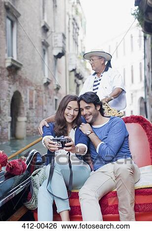 Stock Photograph - Smiling couple taking self-portrait with digital camera in gondola on canal in Venice. Fotosearch
