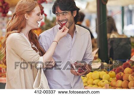 Smiling couple tasting fruit in market View Large Photo Image Stock Photo - Smiling couple tasting fruit in market. Fotosearch