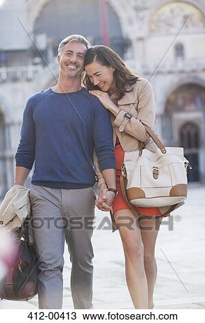 Smiling couple walking through town square View Large Photo Image Stock Image - Smiling couple walking through town square. Fotosearch