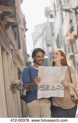 Stock Photo - Smiling couple walking with map on narrow street in Venice. Fotosearch