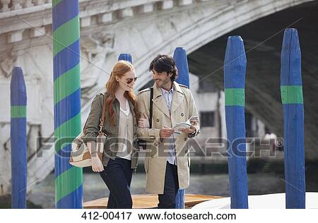 Stock Photo - Smiling couple with guidebook walking in Venice. Fotosearch