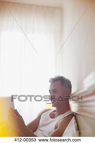 Stock Image - Smiling man using digital tablet in bed. Fotosearch