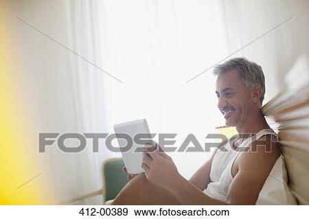 Smiling man using digital tablet in bed View Large Photo Image Stock Photo - Smiling man using digital tablet in bed. Fotosearch