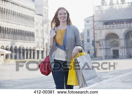 Stock Image - Smiling woman carrying shopping bags through St. Mark's Square in Venic. Fotosearch