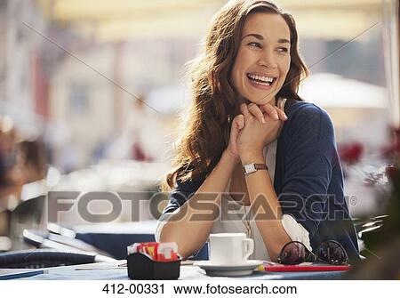 Stock Image - Smiling woman drinking coffee at sidewalk cafe. Fotosearch