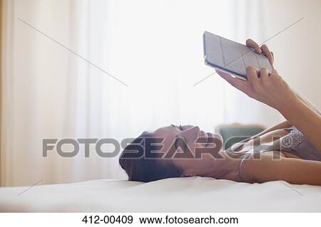 Smiling woman laying on bed and using digital tablet View Large Photo Image Stock Photo - Smiling woman laying on bed and using digital tablet. Fotosearch