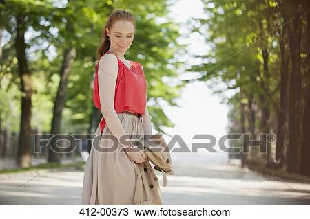Stock Image - Smiling woman looking down in park. Fotosearch