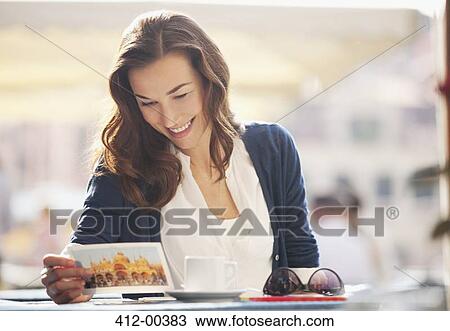 Stock Image - Smiling woman reading postcard at sidewalk cafe. Fotosearch