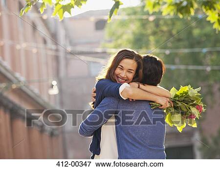 Smiling woman with flowers hugging man View Large Photo Image Stock Photo - Smiling woman with flowers hugging man. Fotosearch
