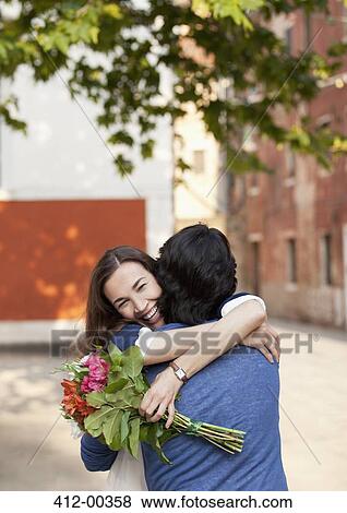 Stock Photo - Smiling woman with flowers hugging man. Fotosearch